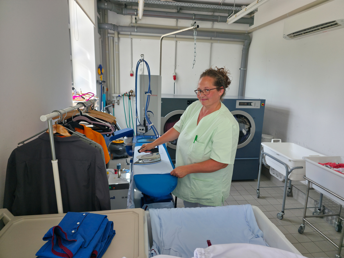 Eine Mitarbeiterin die gerade die Bewohnerwäsche bügelt und dabei in die Kamera lächelt.